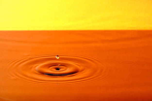 Spruzzare una goccia d'acqua con cerchi d'acqua divergenti su sfondo arancione