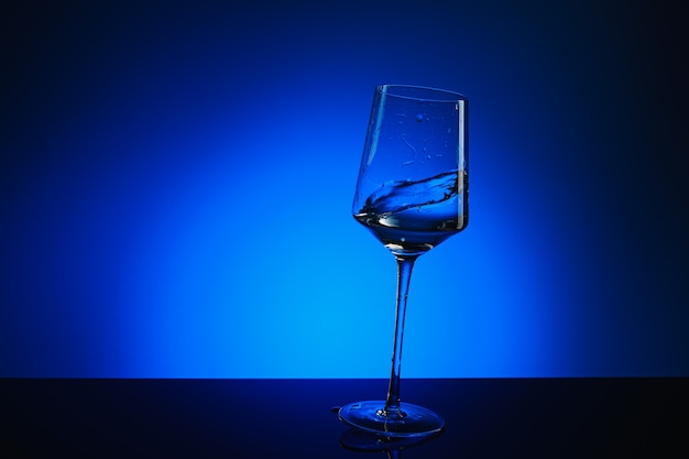 Spruzzata d'acqua in un bicchiere su sfondo blu.