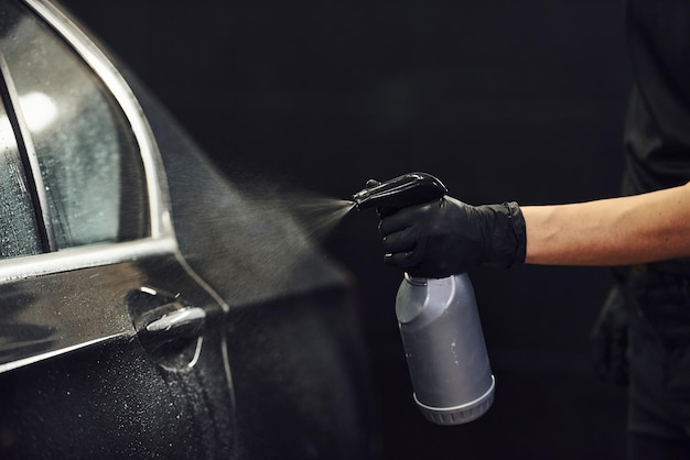 Spruzzatura del veicolo La moderna automobile nera viene pulita da una donna all'interno della stazione di autolavaggio