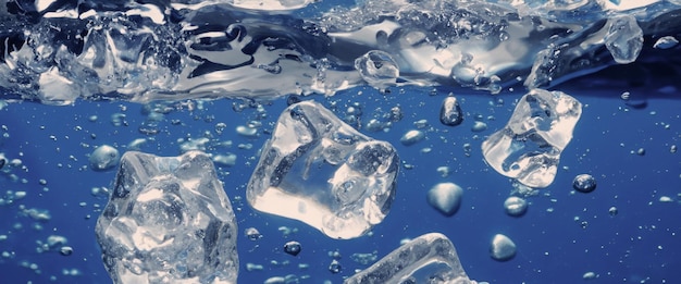 Spruzzi d'acqua e cubetti di ghiaccio Spruzzi di ghiaccio in un bicchiere d'acqua Versare sott'acqua cubetti di ghiaccio che cadono in uno sfondo trasparente e rinfrescante Bere ghiaccio in un bicchiere con sfondo blu