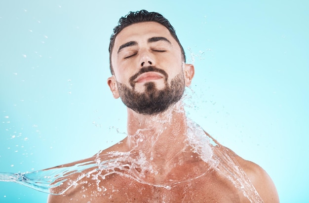 Spruzzi d'acqua e cura della pelle con il volto dell'uomo per la doccia cura di sé e cosmetici naturali Idratazione di lusso e rinfrescante con modello per dermatologia benessere e pulizia in studio sfondo blu