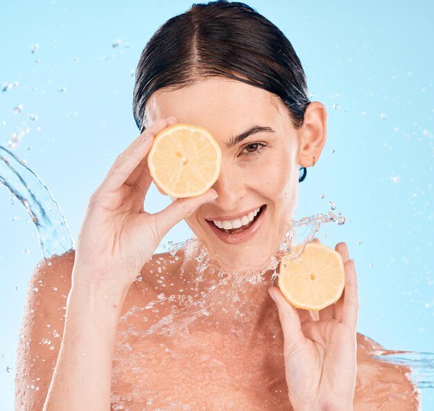 Spruzzi d'acqua limone e ritratto di donna in studio per un trattamento biologico naturale e salutare per la cura della pelle Vitamina c bellezza e modella con agrumi per il benessere del viso e della pelle su sfondo blu