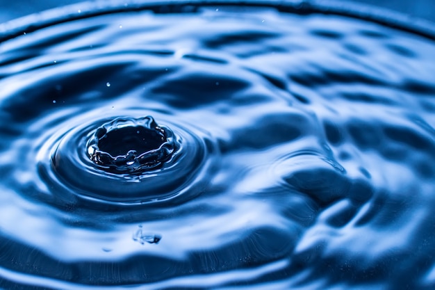 Spruzzi di gocce d'acqua in un bicchiere di colore blu