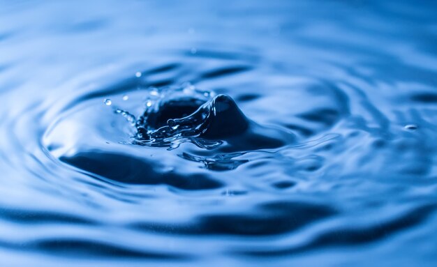 Spruzzi di gocce d'acqua in un bicchiere di colore blu