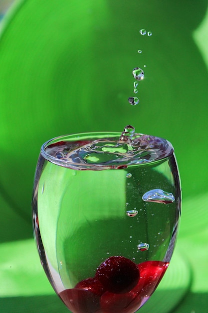 Spruzzi in un bicchiere con acqua e frutti di bosco su uno sfondo verde brillante.