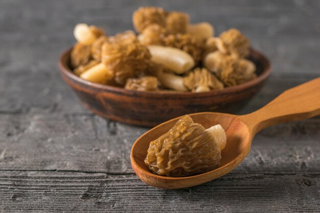 Spugnole fresche in un cucchiaio di legno e una ciotola di argilla su un tavolo di legno I primi funghi primaverili