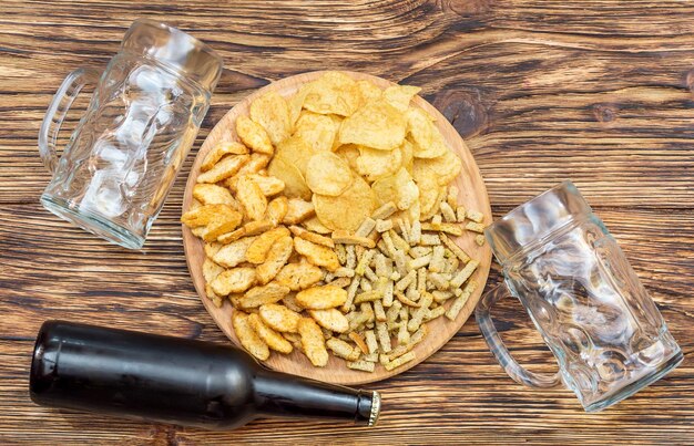 Spuntini salati con bottiglia di birra e due calici vuoti per birra su un tavolo di legno Vista dall'alto