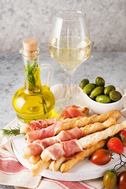Spuntini tradizionali italiani per vino, grissini (grissini), pomodori, prosciutto (jamon), fragole e olive. Messa a fuoco selettiva.