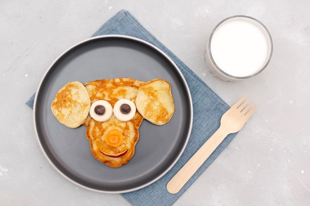 Spuntino a forma di viso divertente cane scimmia da pancakecheese sul piatto Cute bambini bambini dolce dessert colazione sana pranzo cibo arte con milkapples su sfondo grigio cemento vista dall'alto