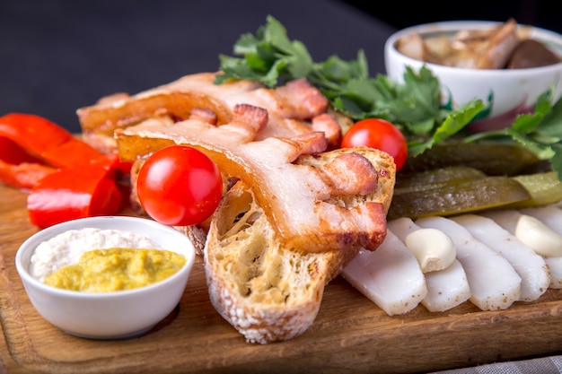 Spuntino con petto fritto, pane, strutto tagliato, pomodori freschi e funghi marinati su tavola di legno. Aperitivo