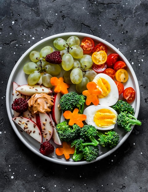 Spuntino creativo per bambini con verdure e frutta in un piatto su uno sfondo scuro vista dall'alto