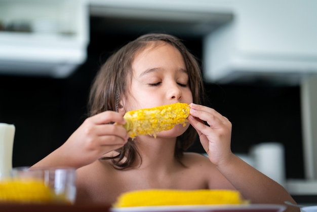 Spuntino estivo, ragazzino seduto e che mangia mais Foto di alta qualità