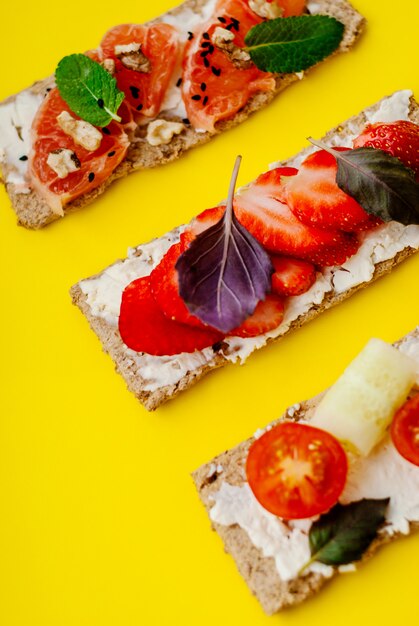 Spuntino sano con pane croccante, crema di formaggio, fragola, pompelmo, pomodoro e cetriolo su uno sfondo giallo