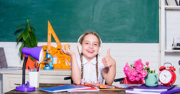 Spuntino tra le lezioni Studentessa sedersi scrivania lavagna sfondo Stile di vita sano Concetto di vita scolastica Infanzia moderna Pausa scolastica Ragazza bambino piccolo che mangia frutta mela Kid studente a scuola