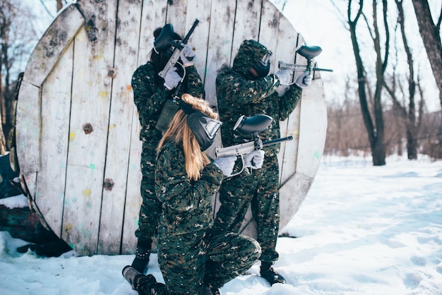 Squadra di paintball in uniforme e maschere che sparano al nemico, vista laterale, battaglia nella foresta invernale. Gioco di sport estremi