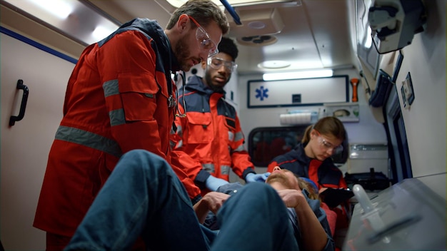 Squadra medica di razza mista che fornisce primo soccorso in ambulanza Paramedico professionista che fornisce soccorso medico al paziente Lavoratore medico che controlla lo stomaco dell'uomo durante le cure di emergenza Concetto di soccorso