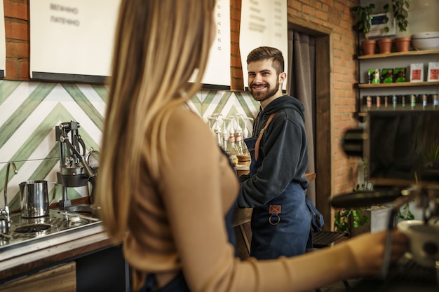 Squadra professionale e felice di barista che prepara caffè usando la macchina del caffè nella caffetteria