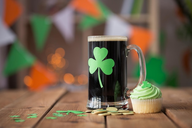 St. Patrick's Day vacanze e celebrazione concetto bicchiere di birra scura con ciambella verde cupcake e monete d'oro su tavolo di legno