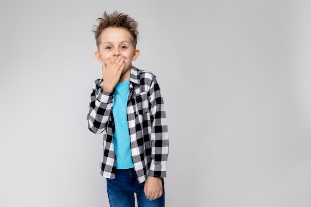 Sta un bel ragazzo in camicia a quadri, camicia blu e jeans. Il ragazzo sorride e si copre la bocca con la mano