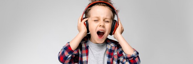 Sta un bel ragazzo in camicia a quadri, camicia grigia e jeans. Un ragazzo in cuffia rossa canta una canzone.