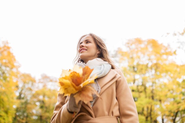stagione e concetto di persone - bella giovane donna con foglie di acero che camminano nel parco autunnale