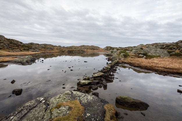 Stagno lungo il sentiero, presso l'arcipelago Rovaer, isola di Haugesund, Norvegia. Pietre che fanno un percorso attraverso l'acqua.