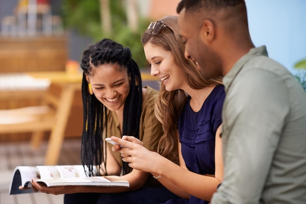 Stampa e digitale nel mondo studentesco Tre amici che leggono un libro e un cellulare seduti all'aperto