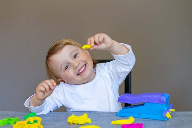 Stampi sorridenti del ragazzino dalla plastilina colorata sul tavolo