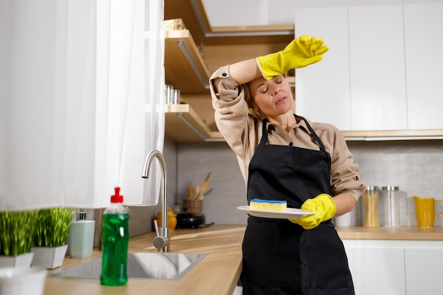 Stanca delle faccende domestiche, la donna lava i piatti in cucina