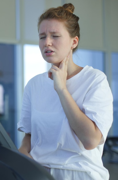 Stanca esausta giovane donna sta allenando l'allenamento in esecuzione sul tapis roulant in palestra tenendo la testa con