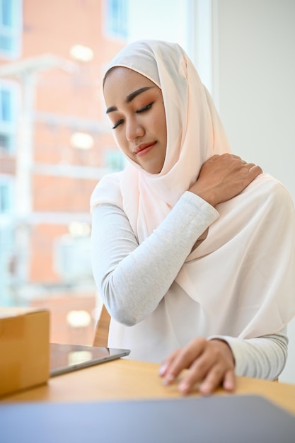 Stanca giovane donna d'affari musulmana asiatica che soffre di dolore alla spalla e alla schiena