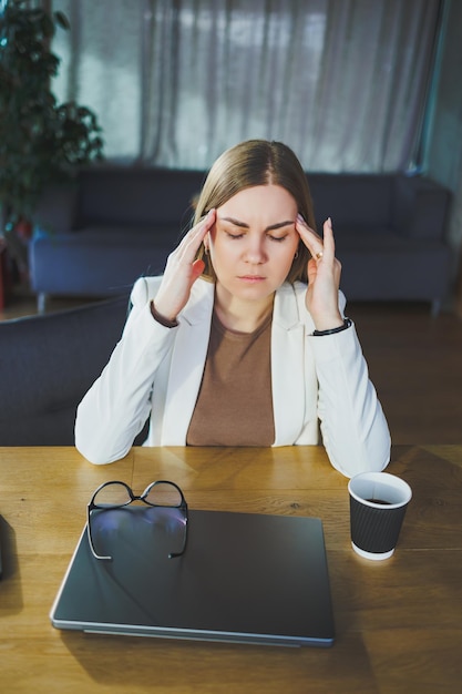 Stanca giovane donna d'affari seduta in ufficio a un tavolo di legno dietro un computer portatile Un giovane manager con gli occhiali è stanco del lavoro