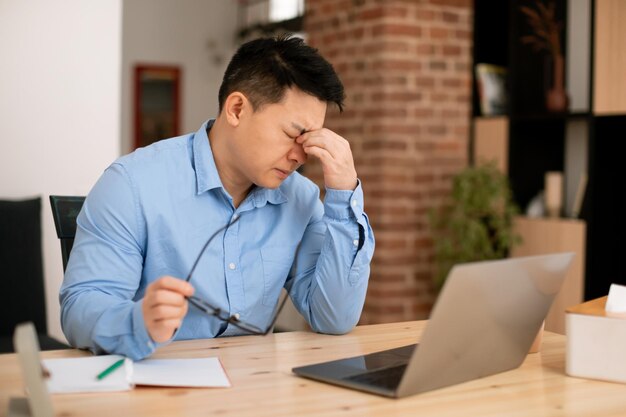 Stanco asiatico libero professionista di mezza età che sente gli occhi affaticarsi dopo aver lavorato al laptop da remoto