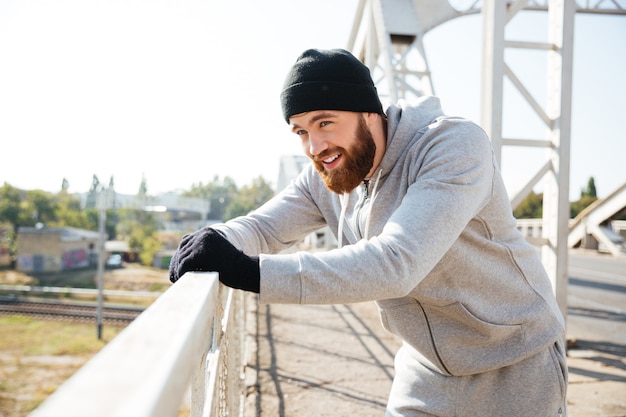 Stanco bel giovane atleta in piedi e in appoggio al ponte urbano