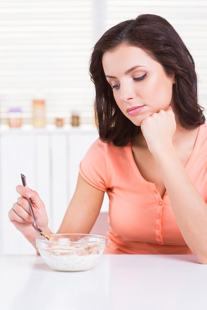 Stanco della dieta. Bella giovane donna che tiene la mano sul mento e guarda la ciotola con i cereali posati sul tavolo della cucina