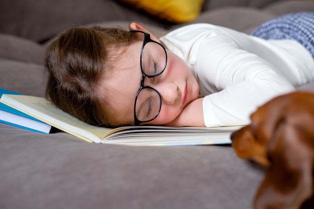 Stanco di studiare e leggere una bambina carina con gli occhiali sta dormendo sul letto su un libro aperto