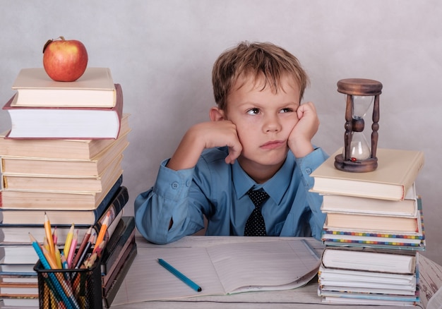 Stanco di studiare ragazzo europeo al tavolo con una montagna di libri, quaderni e matite.isolate