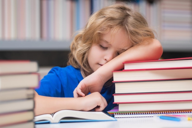 Stanco e annoiato scolaretto bambino legge libri nella biblioteca scolaretto con libro nella biblioteca scolastica ki