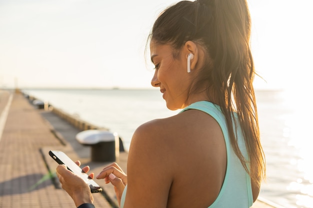 Stanco fitness donna sudorazione prendendo una pausa ascoltando musica sul telefono dopo un allenamento difficile. Giovane donna che ascolta musica con gli auricolari sull'app per smartphone per motivazione fitness