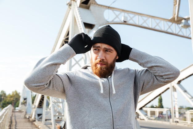 Stanco giovane sportivo con cappello che si prepara per fare jogging mentre si trova sul ponte