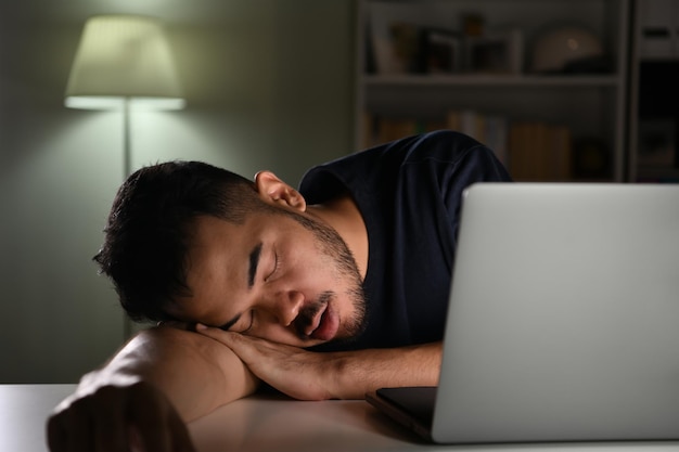 Stanco oberato di lavoro, uomo d'affari asiatico che dorme mentre utilizza il computer che lavora a tarda notte a casa