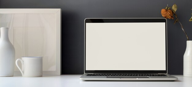 Stanza minima dell'ufficio con il computer portatile aperto dello schermo in bianco con la struttura in bianco