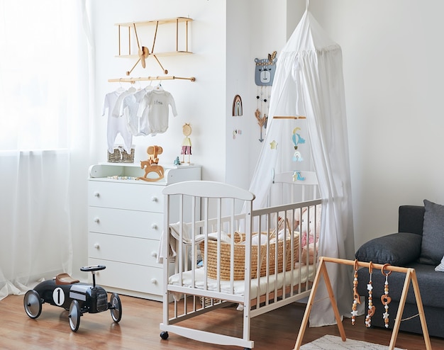 Stanza per bambini interna bianca di stile scandinavo, camera da letto, scuola materna. Culla con â€baldacchino. Scaffali e giocattoli in legno. Simulatore di sviluppo per bambini.