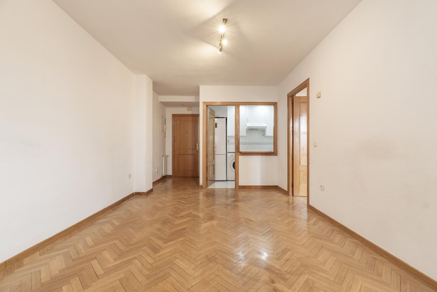 Stanza vuota con porta di accesso sulla strada che accede ad una cucina e portello di servizio, pareti bianche, porte in rovere e pavimenti in parquet a spina di pesce