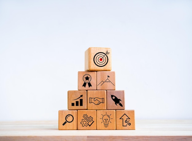 Startup aziendale con crescita processo di successo per il concetto di leadership Piano di obiettivo aziendale e strategia di successo simboli di icone su blocchi di cubo di legno disposti in forma di piramide su sfondo bianco