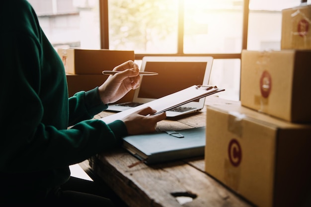 Startup PMI piccola imprenditrice di una donna asiatica freelance che indossa un grembiule che utilizza laptop e scatola per ricevere e rivedere gli ordini online per prepararsi a confezionare vendere ai clienti idee imprenditoriali online per le PMI