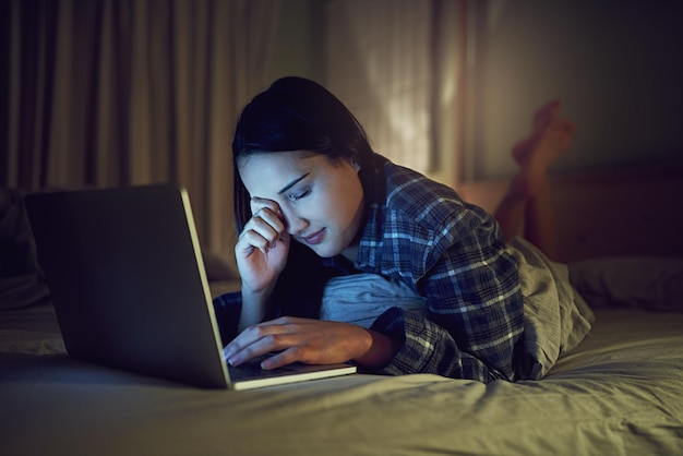 È stata una ripresa online a tarda notte di una giovane donna assonnata che usa un laptop a tarda notte mentre era sdraiata sul letto nella sua camera da letto