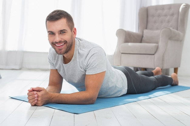 Stato d'animo positivo. Allegro uomo felice che ti sorride mentre giaceva sul materassino yoga