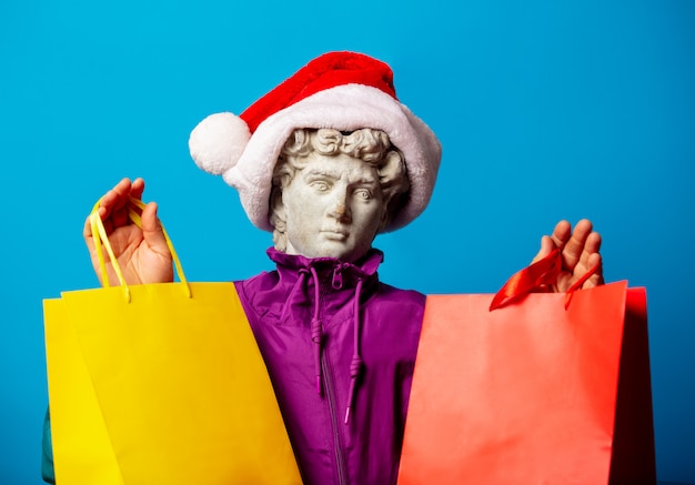 Statua antica vestita con abiti alla moda degli anni novanta e cappello di Babbo Natale con borse della spesa