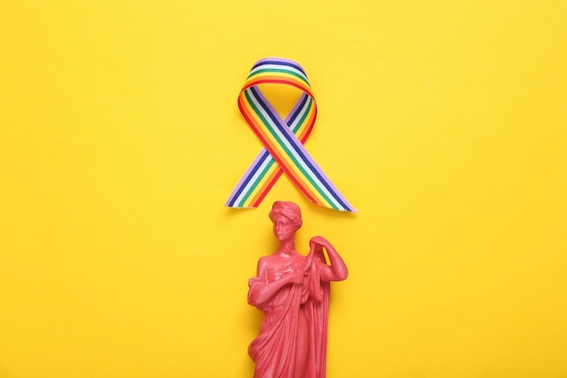 Statua della dea greca antica con simbolo del nastro dell'orgoglio del nastro arcobaleno LGBT su sfondo giallo Vista dall'alto